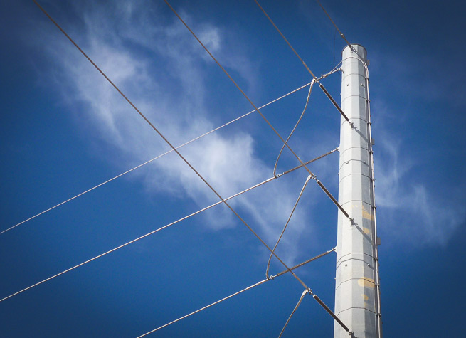 Transmission line pole with blue sky and wispy cloud in background.
